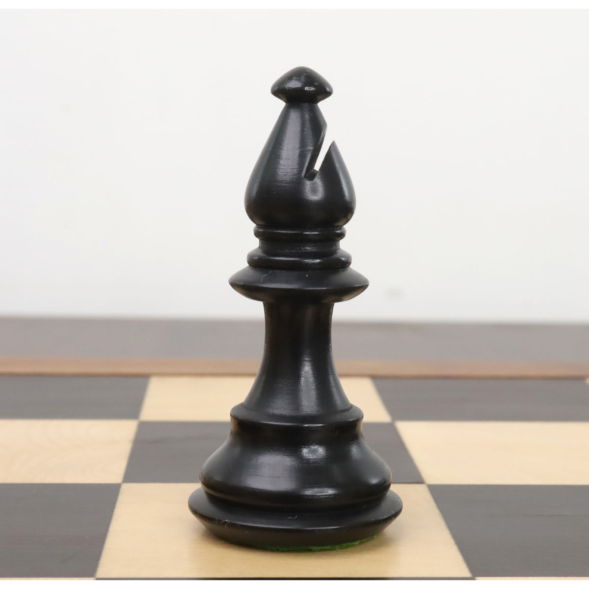 Black ebonised bishop from the 3.7" British Staunton weighted chess set resting on a chessboard.