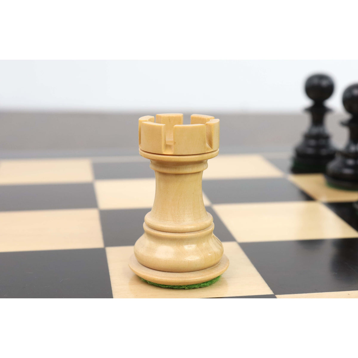 Hand-carved boxwood Rook chess piece with traditional crenellations on a chess board.