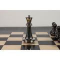 Shiny silver brass metal luxury chess piece Queen on a checkered chess board with blurred background pawns.