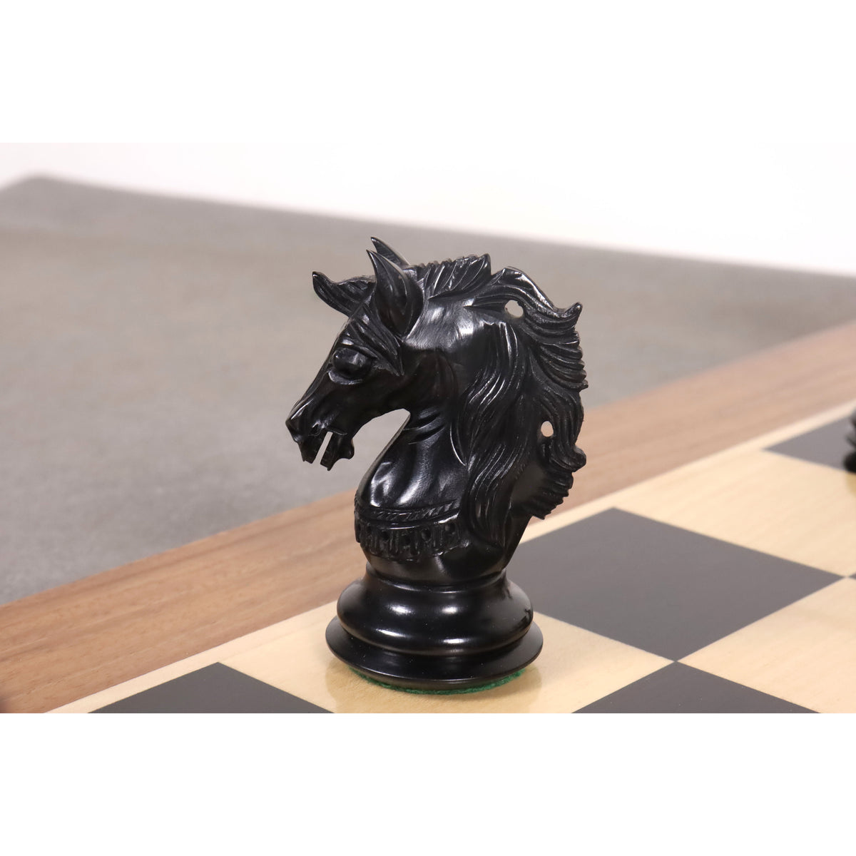 A detailed profile view of a handcrafted ebony Staunton knight on a wooden chessboard.