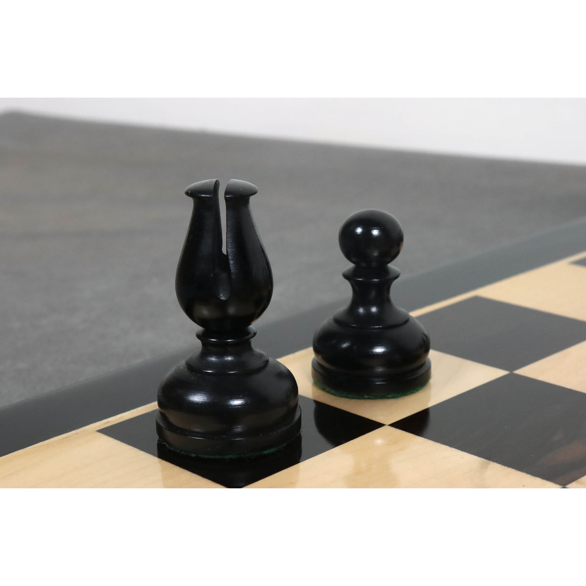 Close-up of a black ebonised Bishop and Pawn on a premium wood chessboard.
