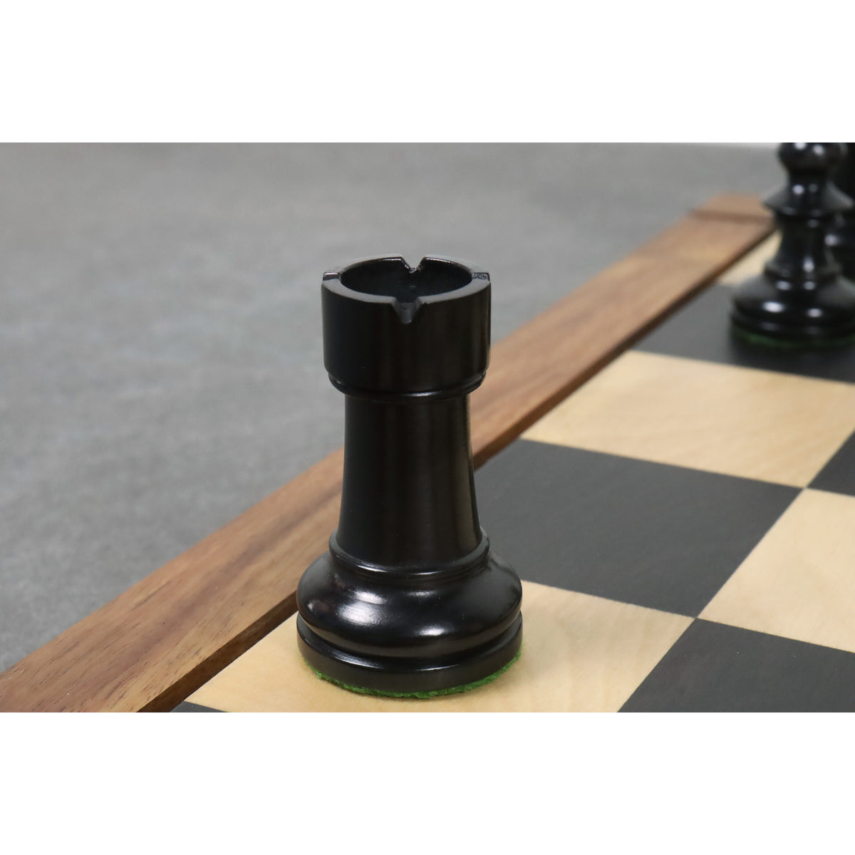 A black ebonized boxwood W.T. Pinney Staunton rook featuring deep turret cuts on a chessboard.