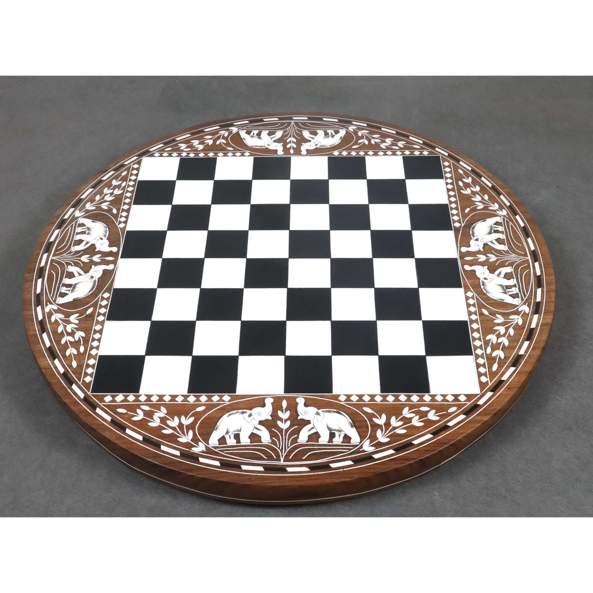 Top view of a round sheesham wood chess board featuring intricate white acrylic elephant and leaf engravings.