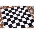 Close-up of the smooth black and ivory acrylic playing squares on a round handcrafted wooden chess board.