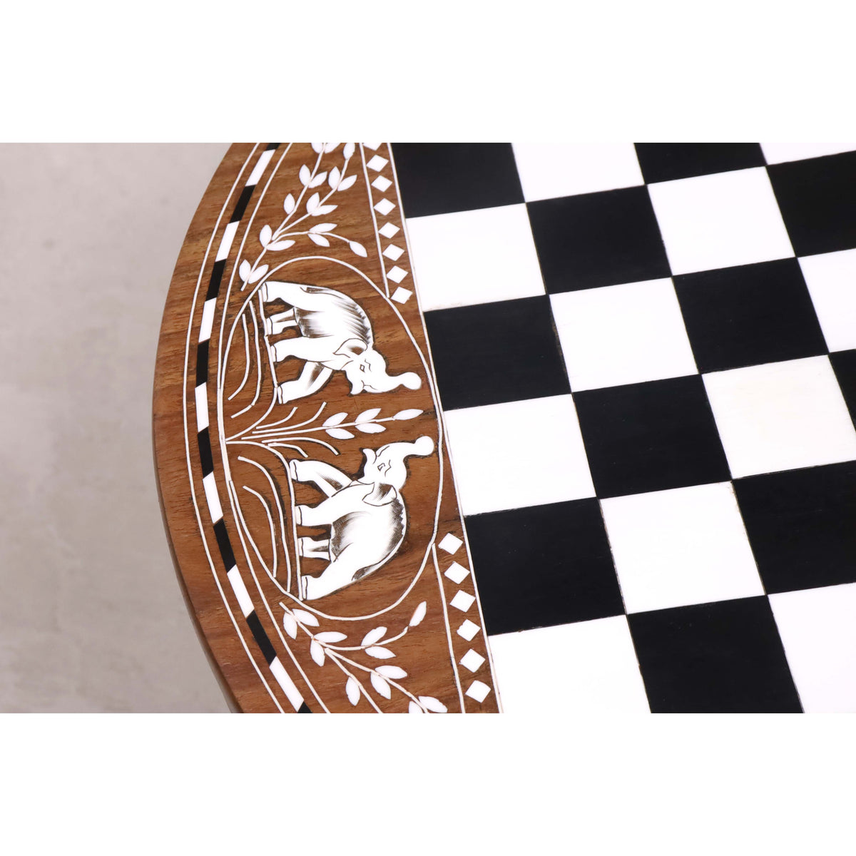 Intricate elephant engravings and geometric diamond inlays on the border of a rosewood chess table.