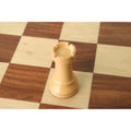 Boxwood French Grandmaster rook piece standing on a wooden chessboard.