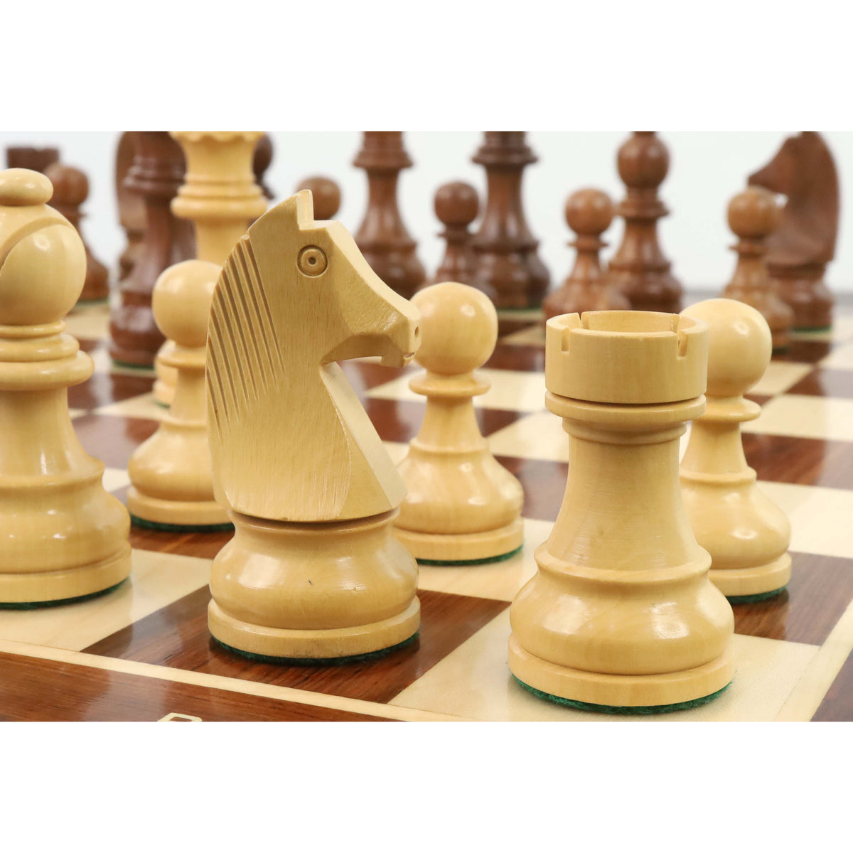 Low-angle close up of a carved boxwood knight and rook piece on a gloss-finish wooden chess board.