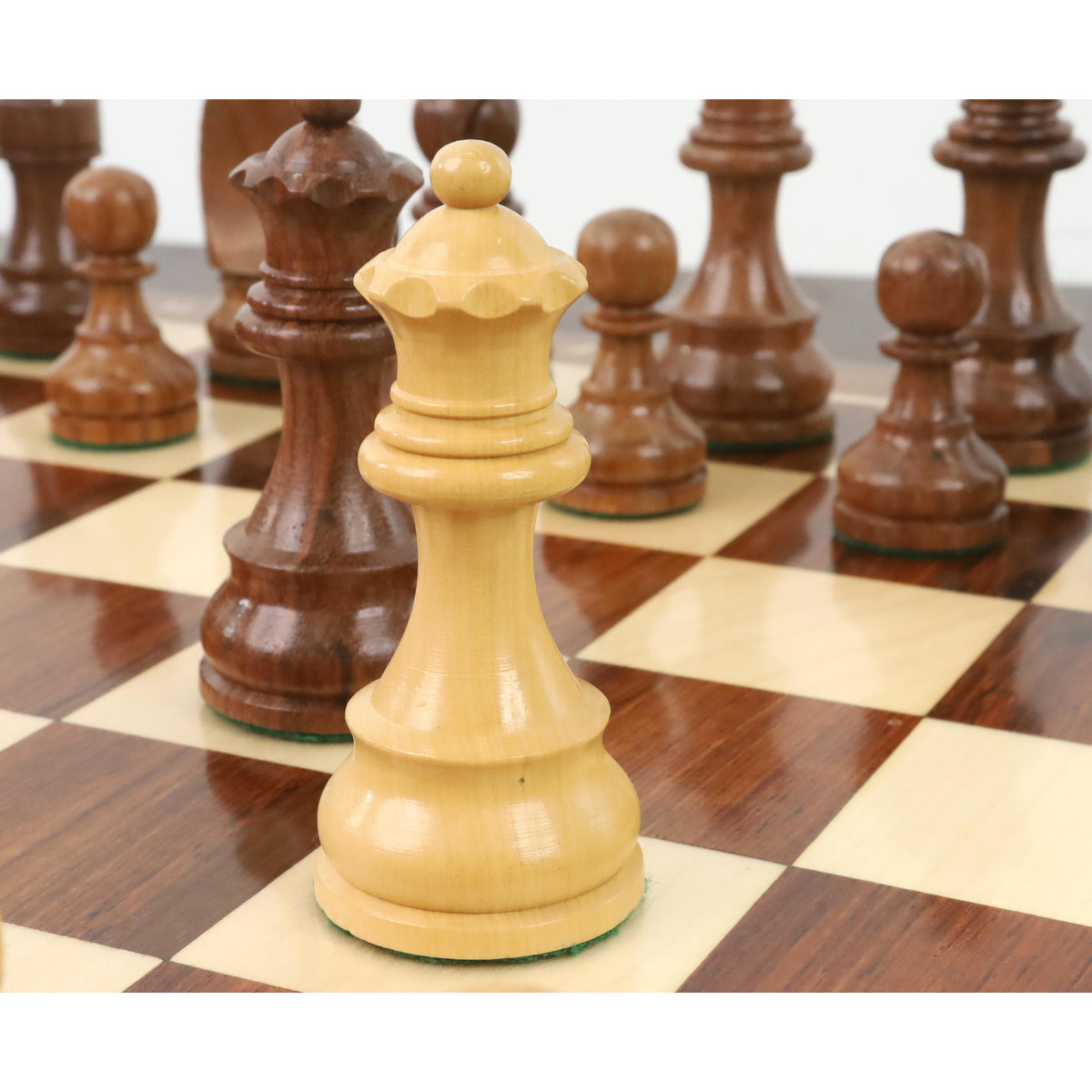 Close-up of a premium boxwood queen piece standing on a wooden chess board with a shallow depth of field.