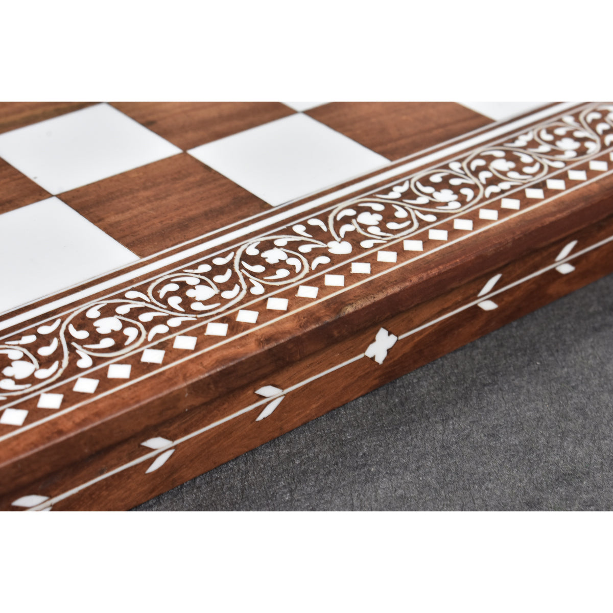 Intricate floral border and leaf motif carvings on an artisanal golden rosewood chess board.