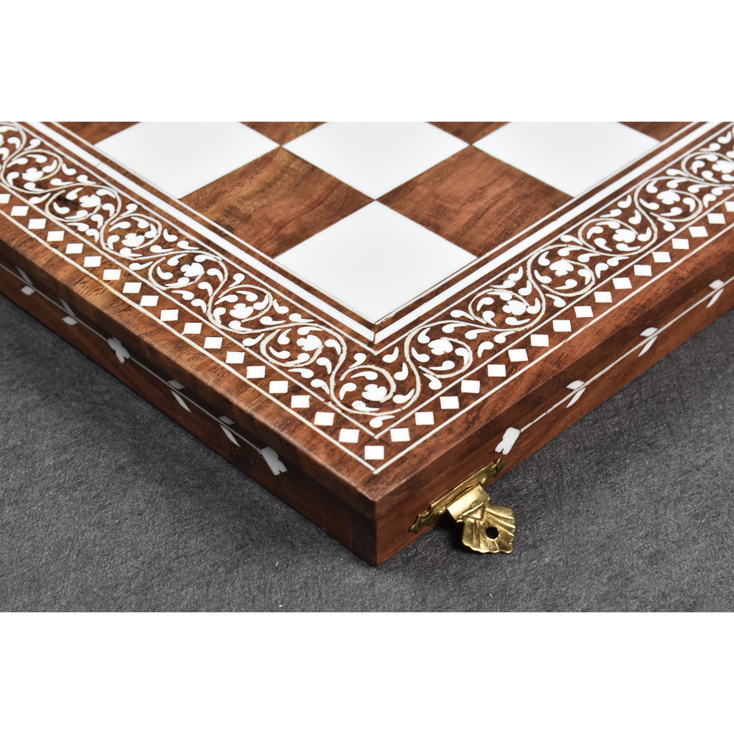 Close-up of artisanal faux ivory floral inlay and brass clasp on a golden rosewood chess board.