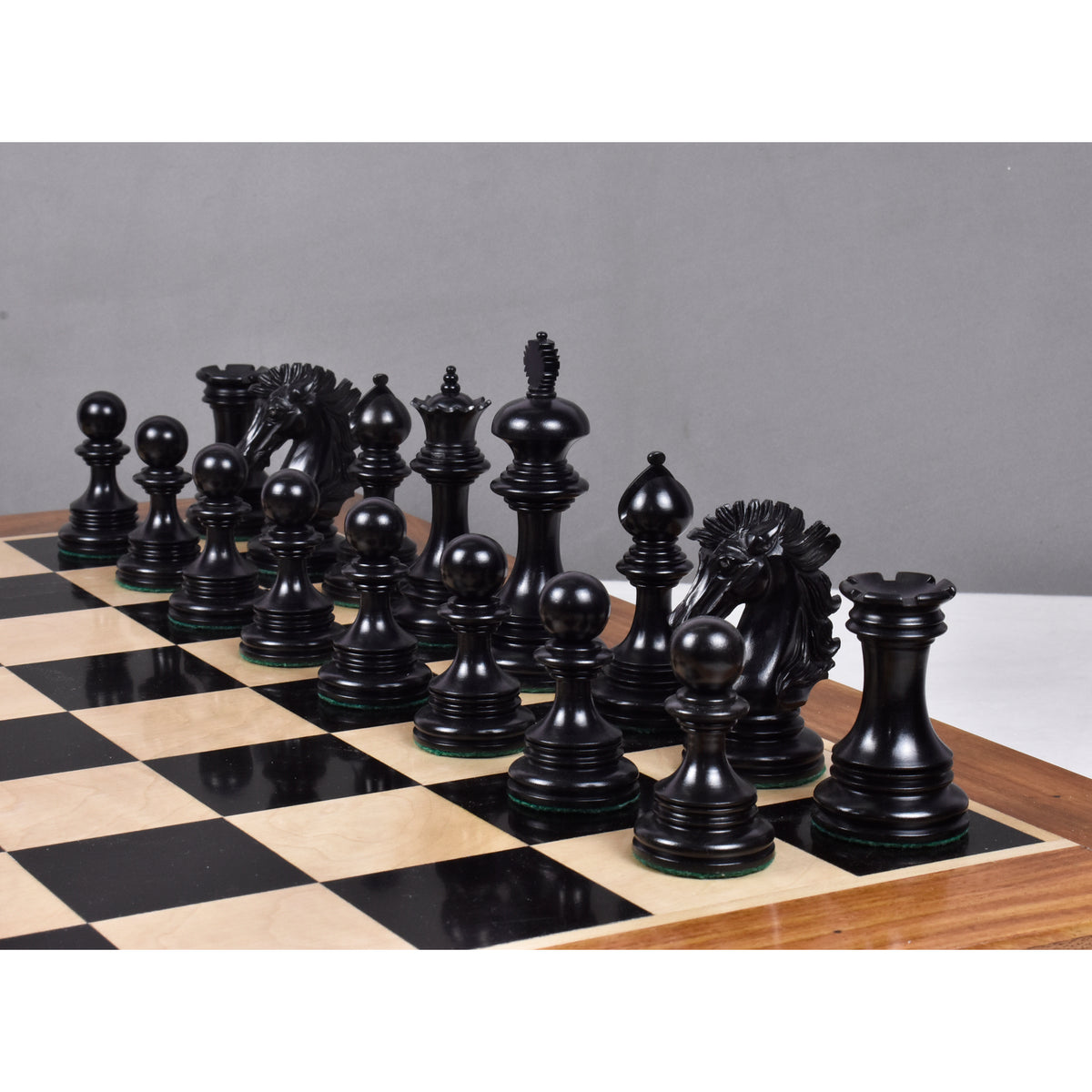 Deep black ebony wood Alexandria luxury Staunton chess pieces set up along the ranks of a glossy wooden board.