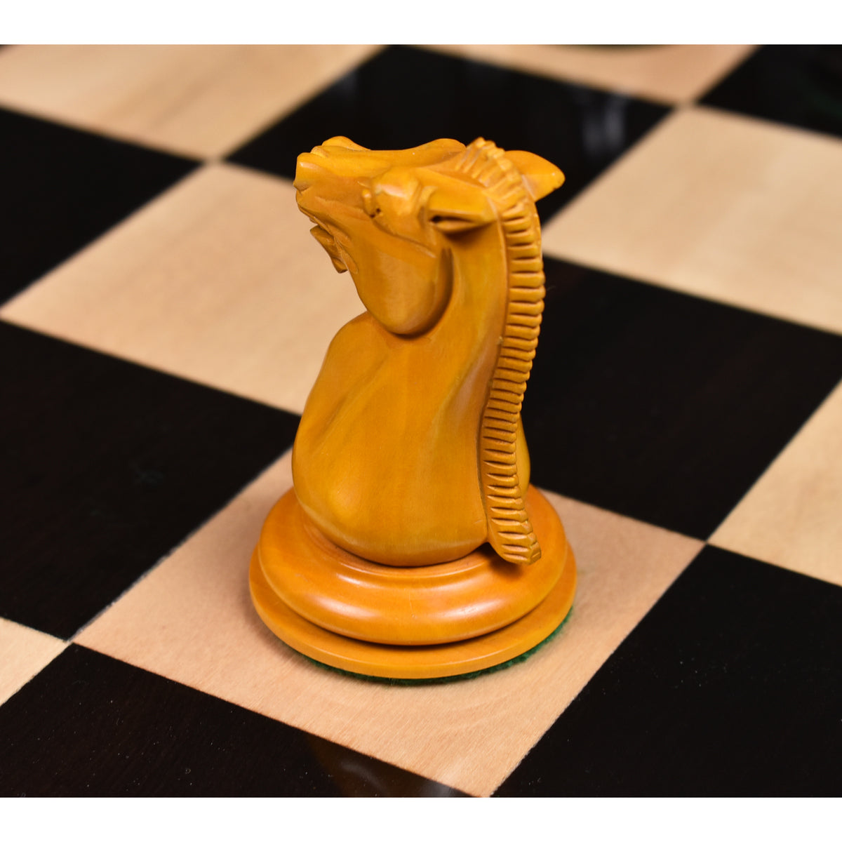 Profile of an antiqued boxwood knight piece showing detailed mane carvings on a black and white chess board.