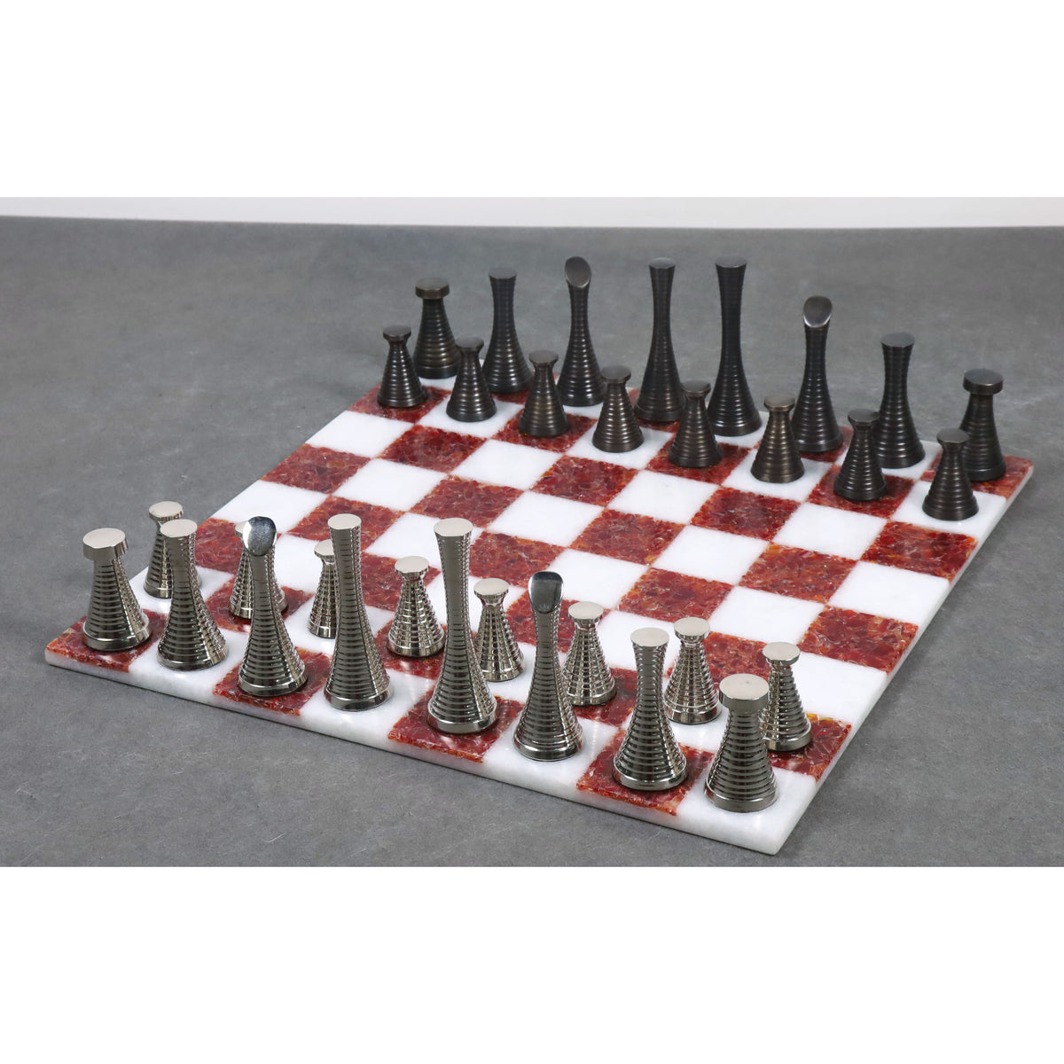 Modern metal chess pieces arranged on a 15 inch red and white marble stone board.