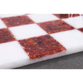 Polished surface of a red and white stone chess board reflecting light on the marble squares.