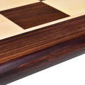 Macro view of the polished rounded edge and border of a rosewood and maple wood chess board.